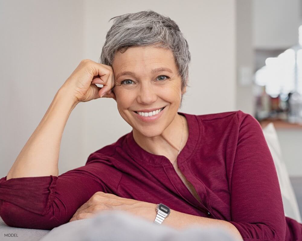 Mature Woman With Wide Smile Sitting On Couch after her all on 4 dental implants procedure
