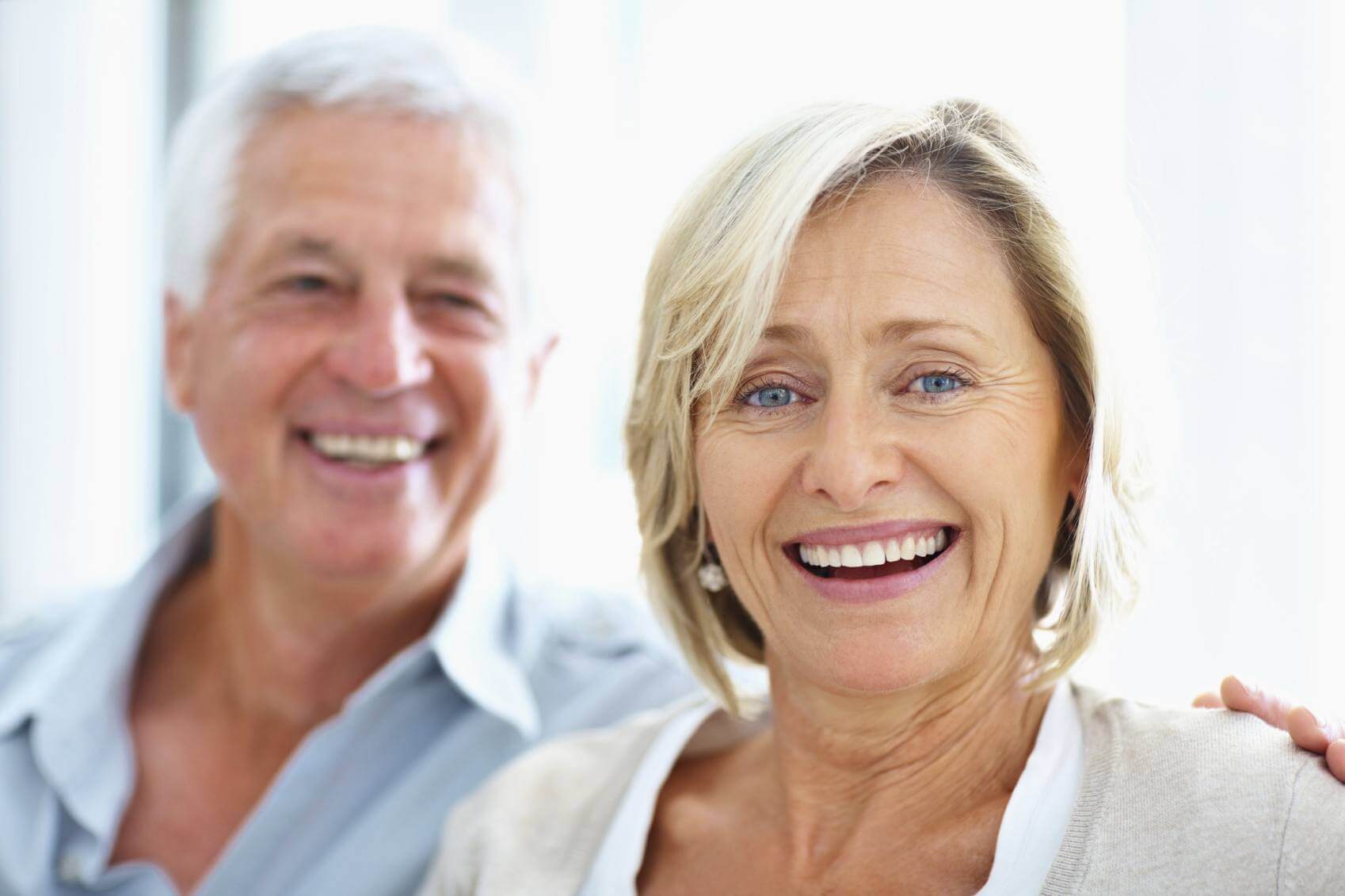 Mature Female Smiling With Blurred Mature Male Behind Her With His Hand On Her Shoulder Copy