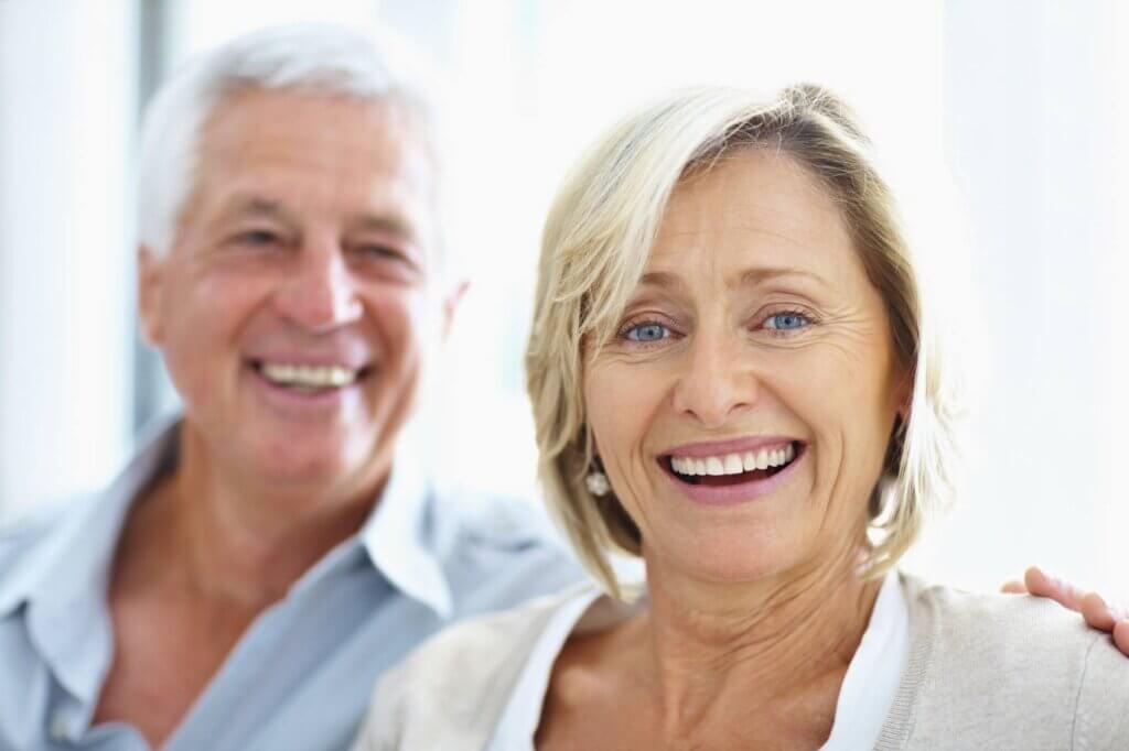 Mature Female Smiling With Blurred Mature Male Behind Her With His Hand On Her Shoulder Copy 2