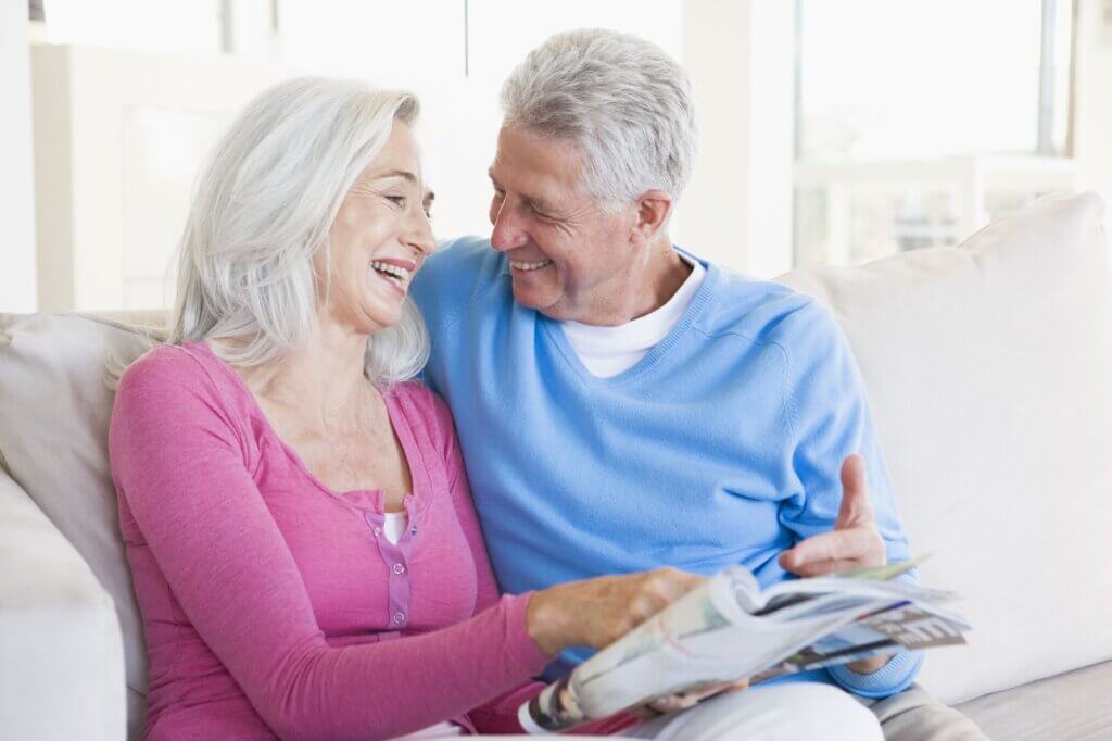 Mature Couple Smiling About Magazine Article While Sitting On Couch