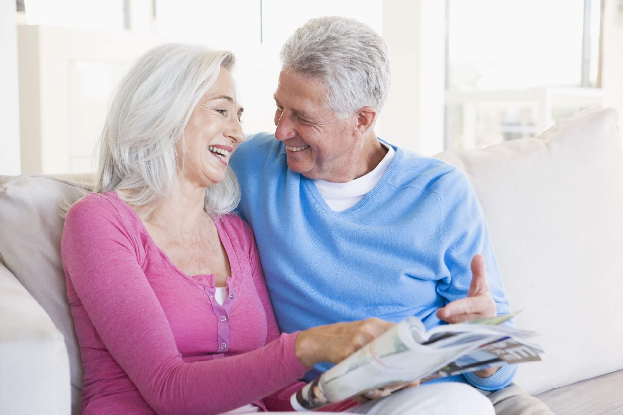 Mature Couple Smiling About Magazine Article While Sitting On Couch