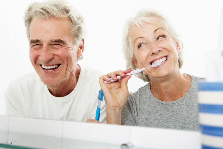 Mature Couple Brushing Teeth In Mirror Reflection